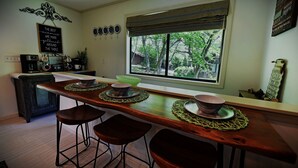 Une cuisine avec un bar en bois, des tabourets, une machine à café et une fenêtre donnant sur les arbres.