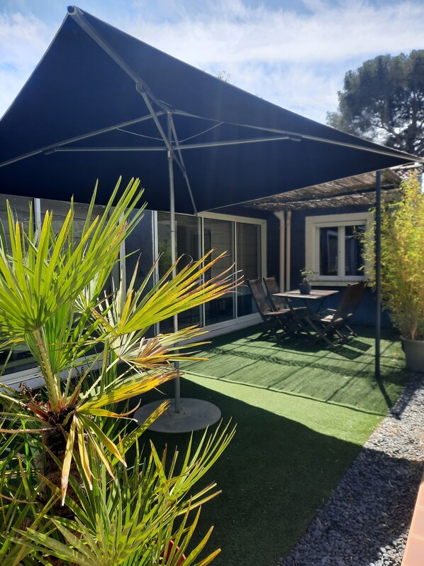 A patio area with artificial grass, a table and chairs, and a large umbrella. - Maison de Vacances, Dans un Écrin de Verdure, Près de la mer (La Garde)
