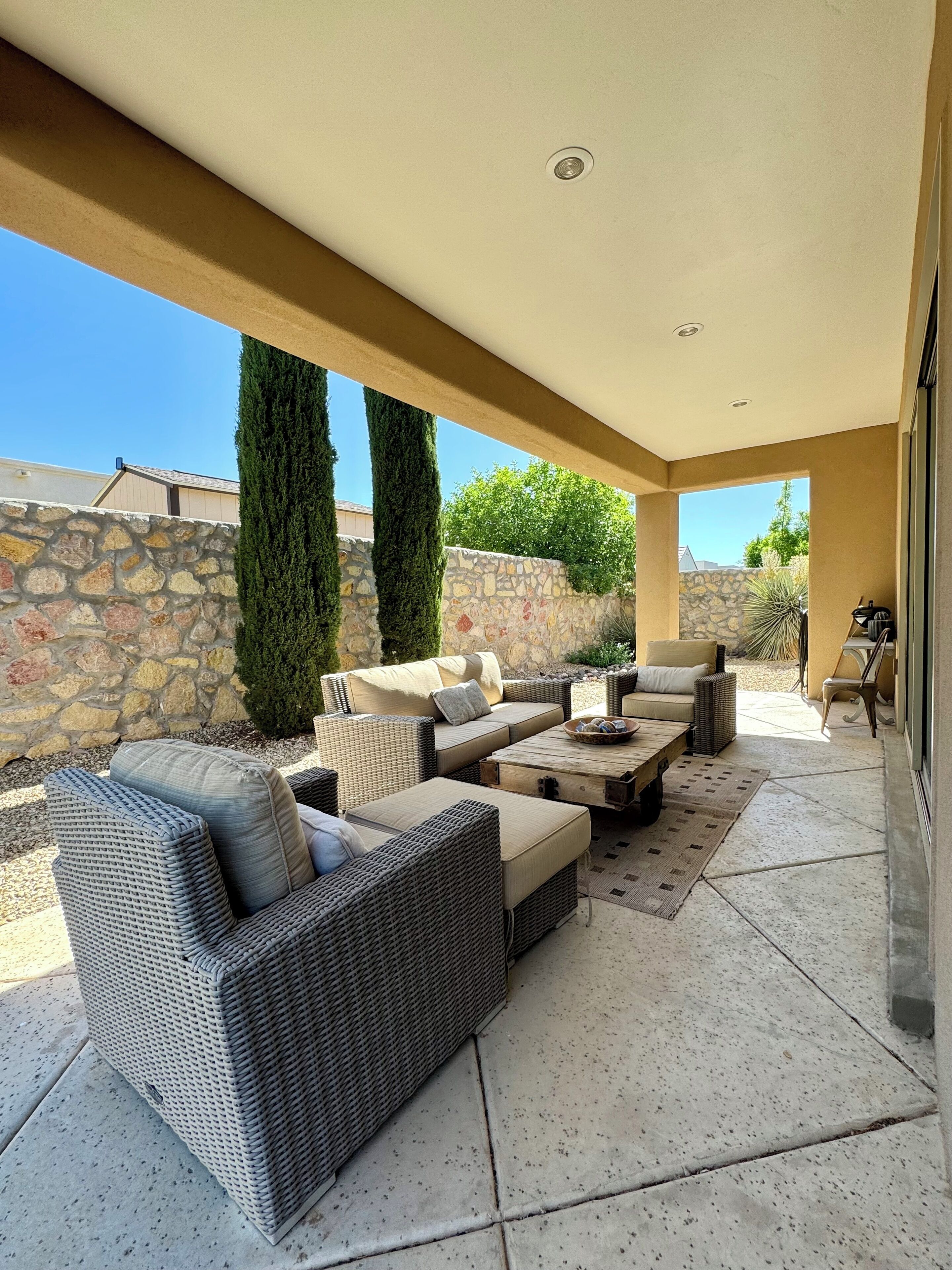 An outdoor patio area with wicker furniture, a stone wall, and a view of the surrounding landscape.