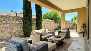 An outdoor patio area with wicker furniture, a stone wall, and a view of the surrounding landscape. - Sweet Sienna Retreat (Las Cruces)