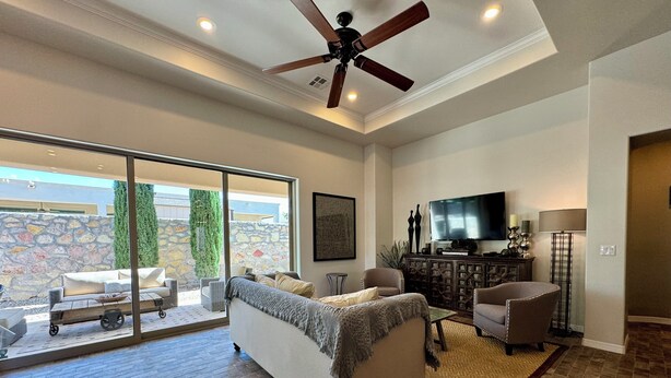 A spacious living room with a large sofa, a television, and a ceiling fan. There is a stone wall and a view of the outdoors. - Sweet Sienna Retreat (Las Cruces)