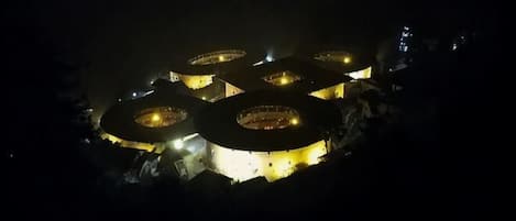 A circular building structure with multiple levels, illuminated by internal lighting.
