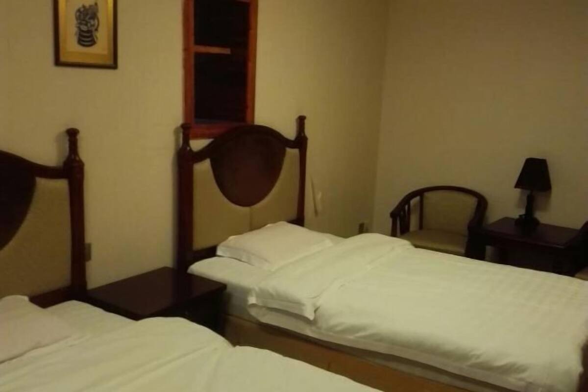 Habitació d'hotel amb dos llits individuals, un panell de fusta al capçal, una taula petita, una cadira i una tauleta de nit.
