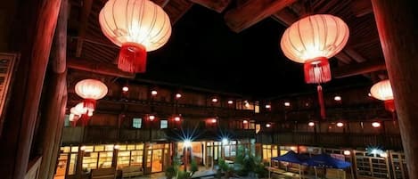 An outdoor courtyard with wooden structures, lanterns, and tables.