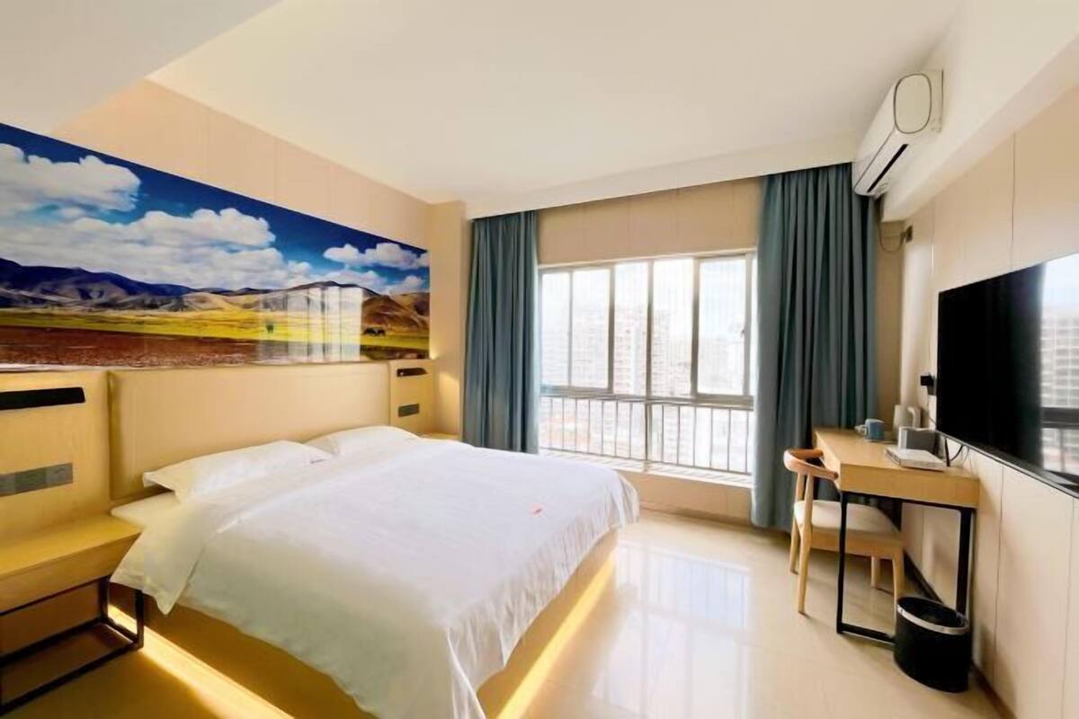 Una habitación de hotel con cama, escritorio, silla, televisor y un amplio ventanal.