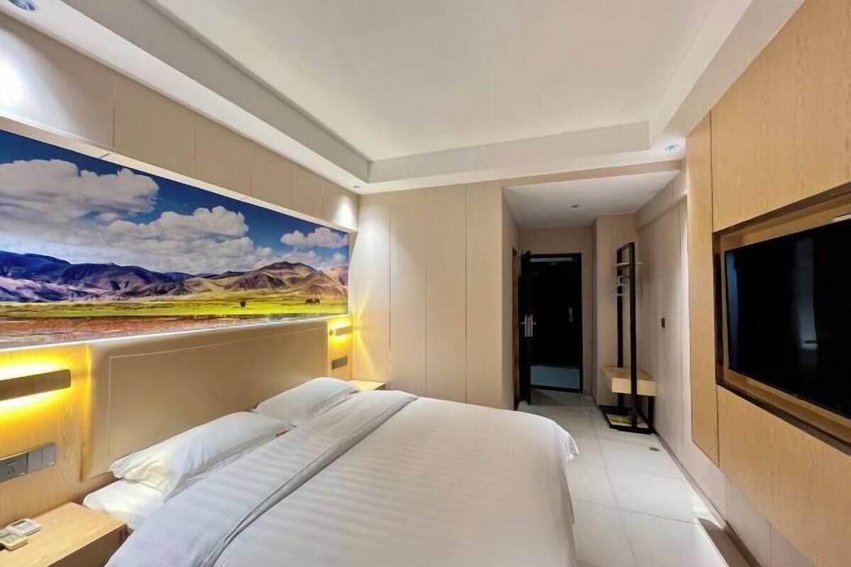 Habitación de hotel con cama, televisión, cuadro de un paisaje y puerta que da a otra habitación.