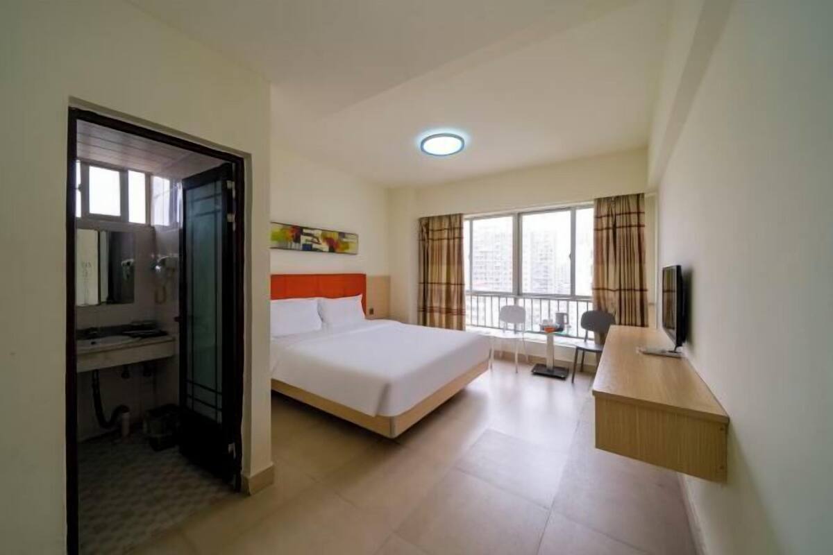 Una habitación de hotel con una cama, un escritorio, un televisor y una ventana con cortinas.
