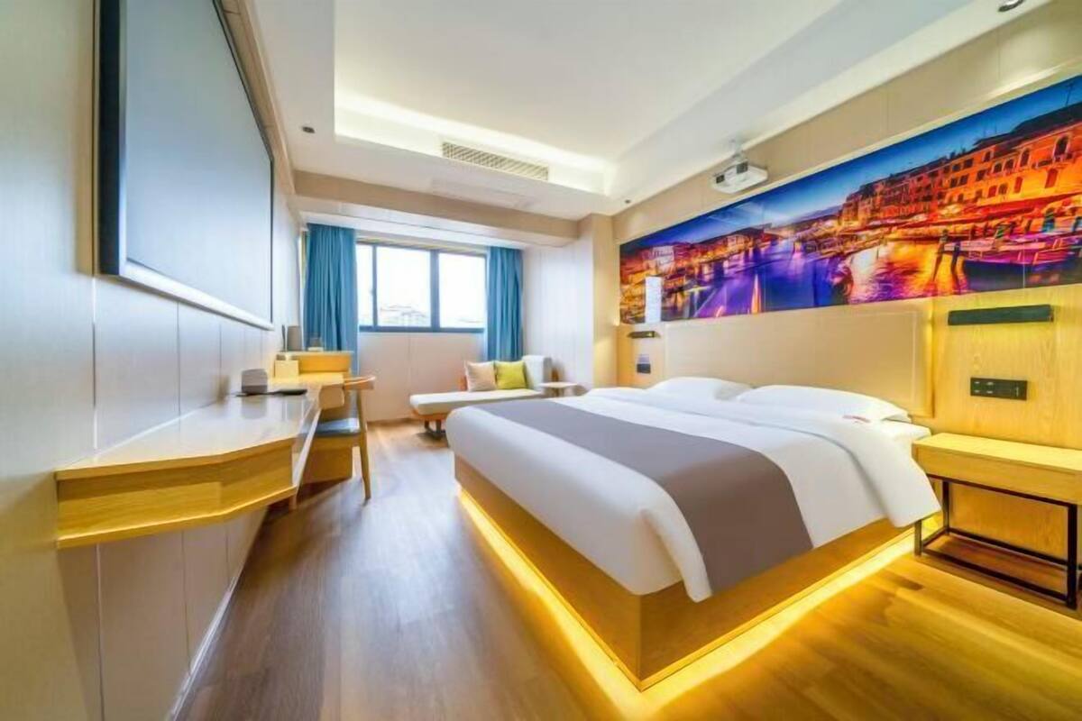 Habitación de hotel moderna con una cama grande, mesitas de noche, un escritorio y un ventanal con cortinas.