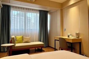 Una habitación de hotel con cama, escritorio, silla, mesita pequeña y sofá.