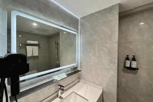 A modern bathroom with a large mirror, a sink, and a shower area.