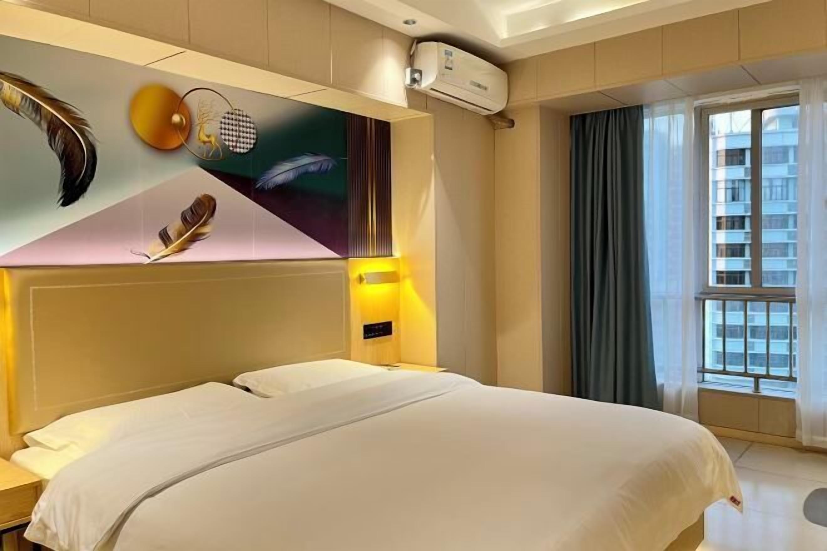 Una habitación de hotel con una cama grande, aire acondicionado en la pared y una ventana con cortinas.