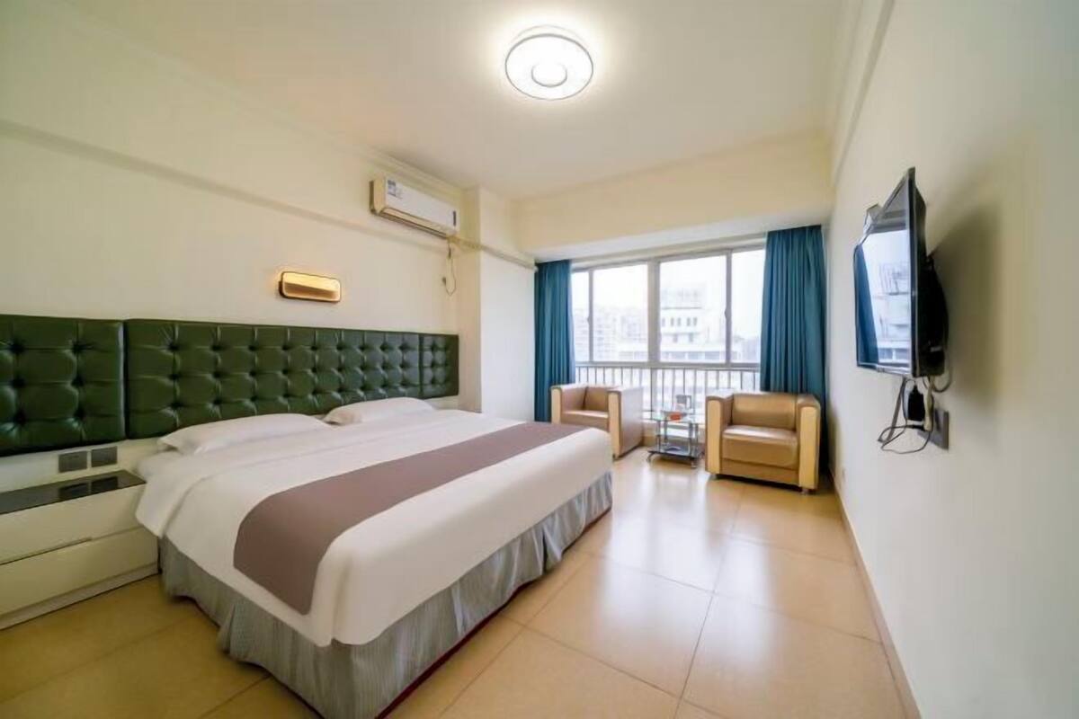Habitación de hotel con una cama grande, televisión, escritorio con silla y balcón con vista a la ciudad.