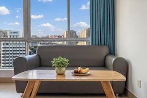 Una sala moderna con un sofá gris, una mesa de centro de madera, una planta en maceta y un plato de fruta.
