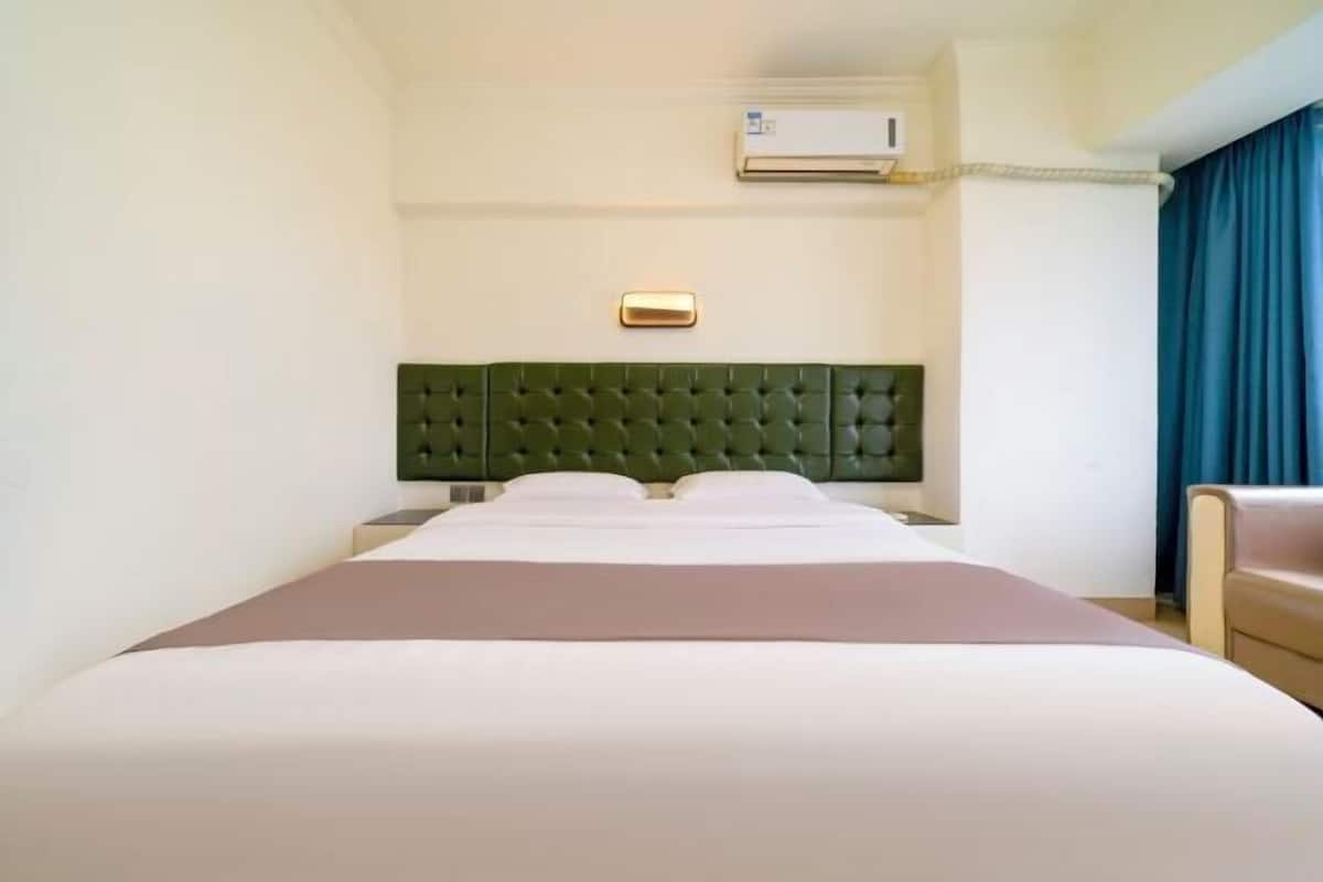 Hotellihuone, jossa on sänky, sängynpääty, ilmastointilaite, yöpöytä ja tuoli.