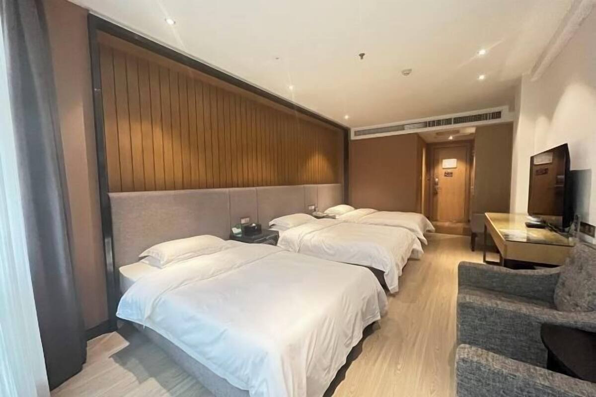 Une chambre d’hôtel avec trois lits, une télévision, un bureau et une chaise.