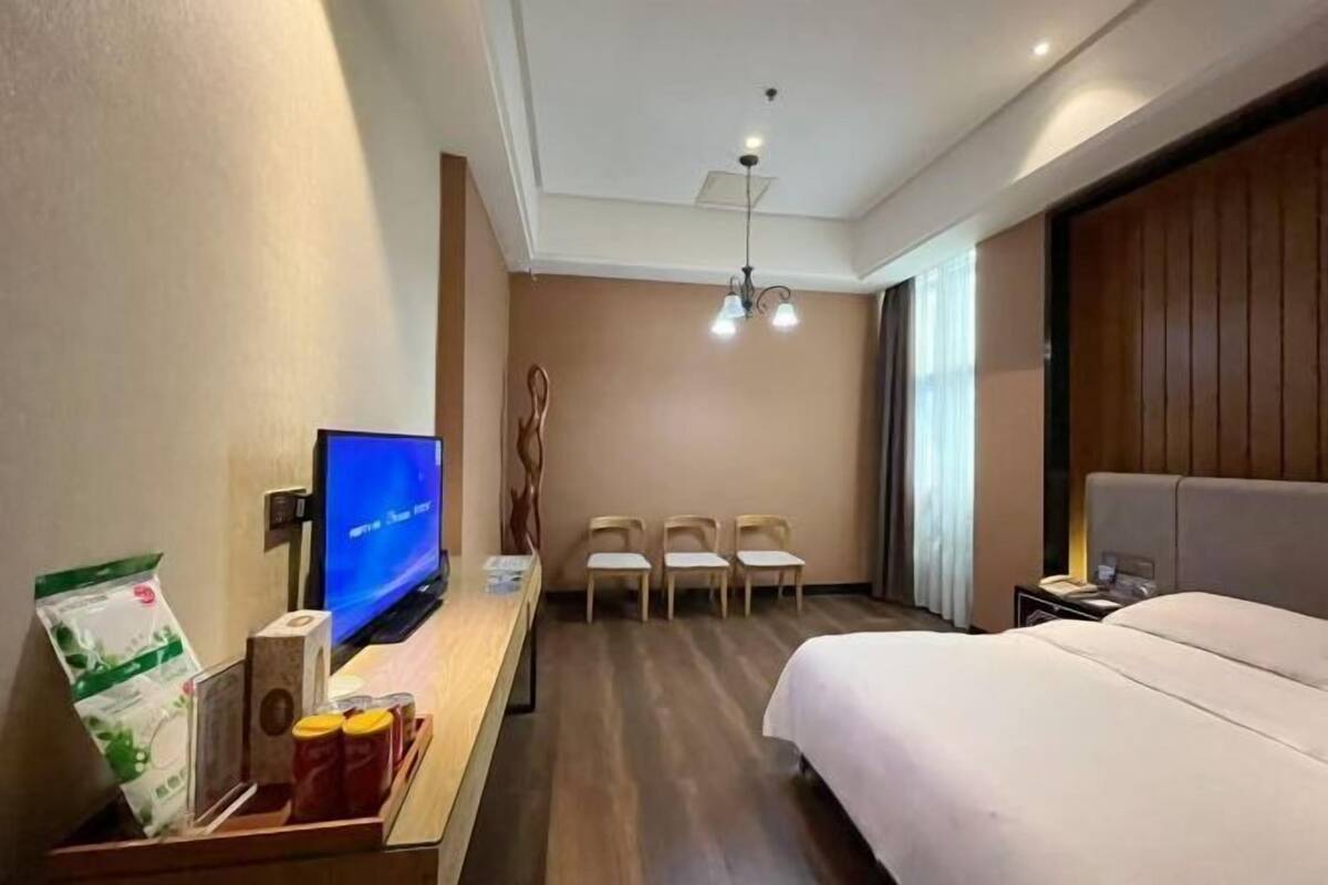 Une chambre d’hôtel comprenant un lit, une télévision, un bureau avec une chaise, une petite table avec quelques objets, et une fenêtre avec des rideaux.