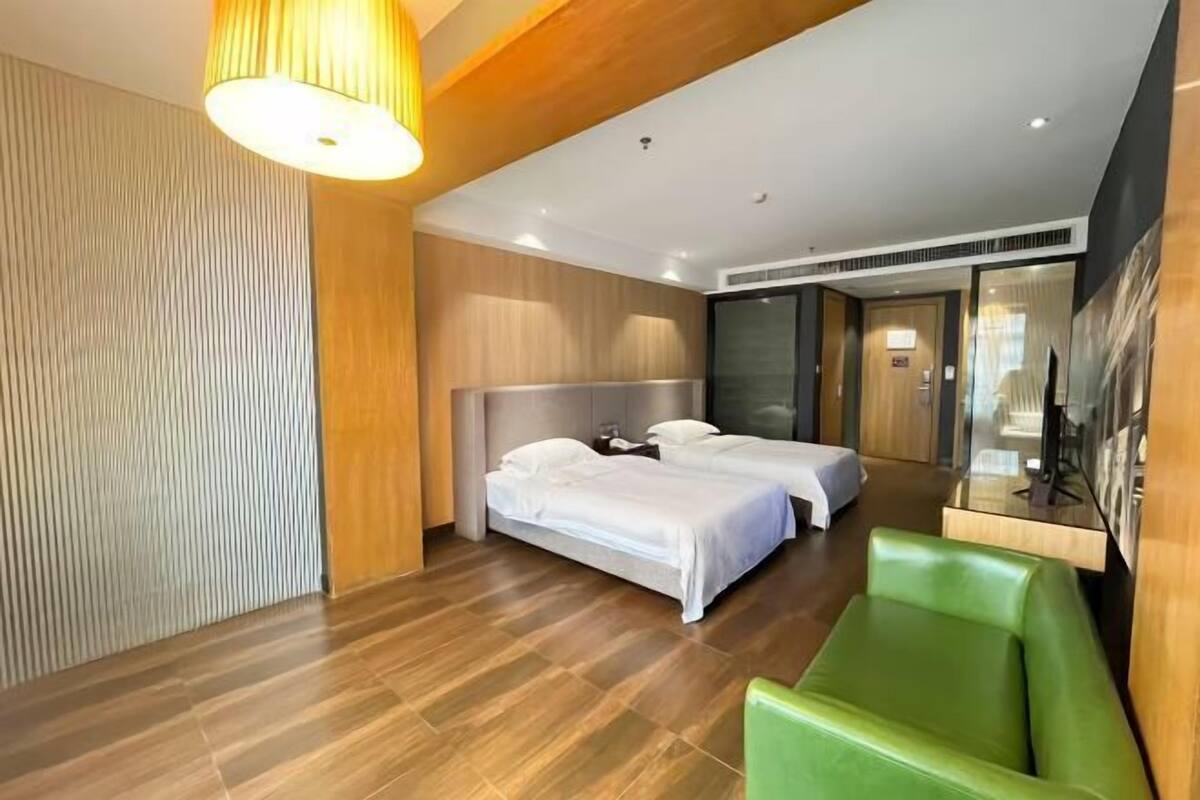 Une chambre d’hôtel avec deux lits, un fauteuil vert, un plafond en bois et une grande fenêtre.