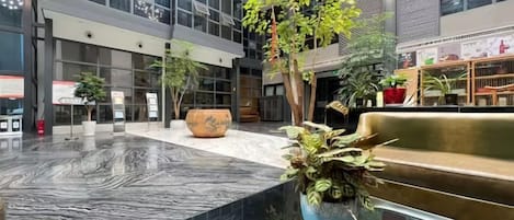 A spacious indoor area with a marble floor, seating areas, and potted plants.