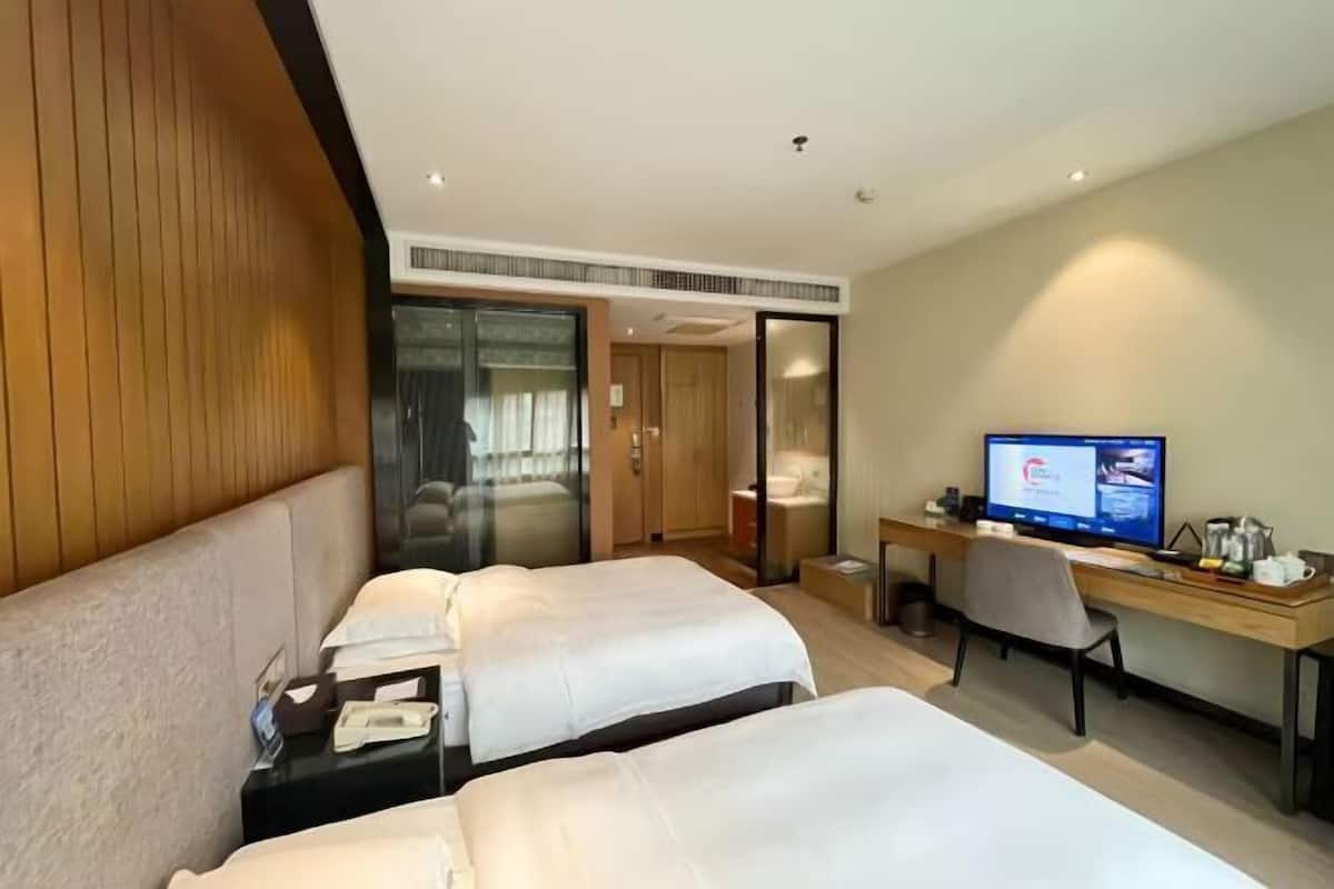 Une chambre d’hôtel avec deux lits, un bureau, une télévision et une porte coulissante donnant accès à la salle de bain.