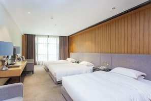 A hotel room with two beds, a desk, a chair, a TV, and a large window with curtains.