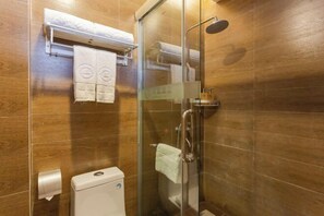 A glass-enclosed shower with a handheld showerhead, a towel rack with folded towels, and a toilet with a paper towel dispenser.