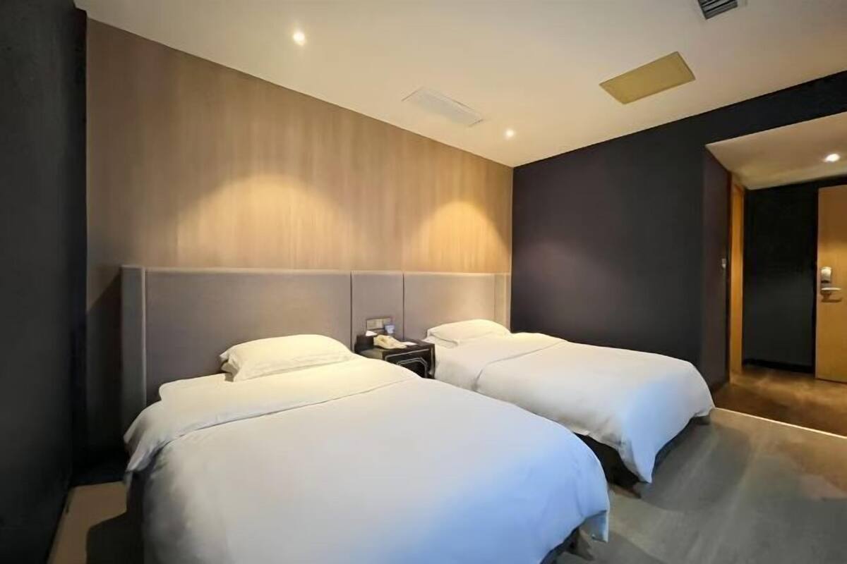 Une chambre d’hôtel avec deux lits, une tête de lit en bois, une petite table de chevet et une porte donnant sur une autre pièce.