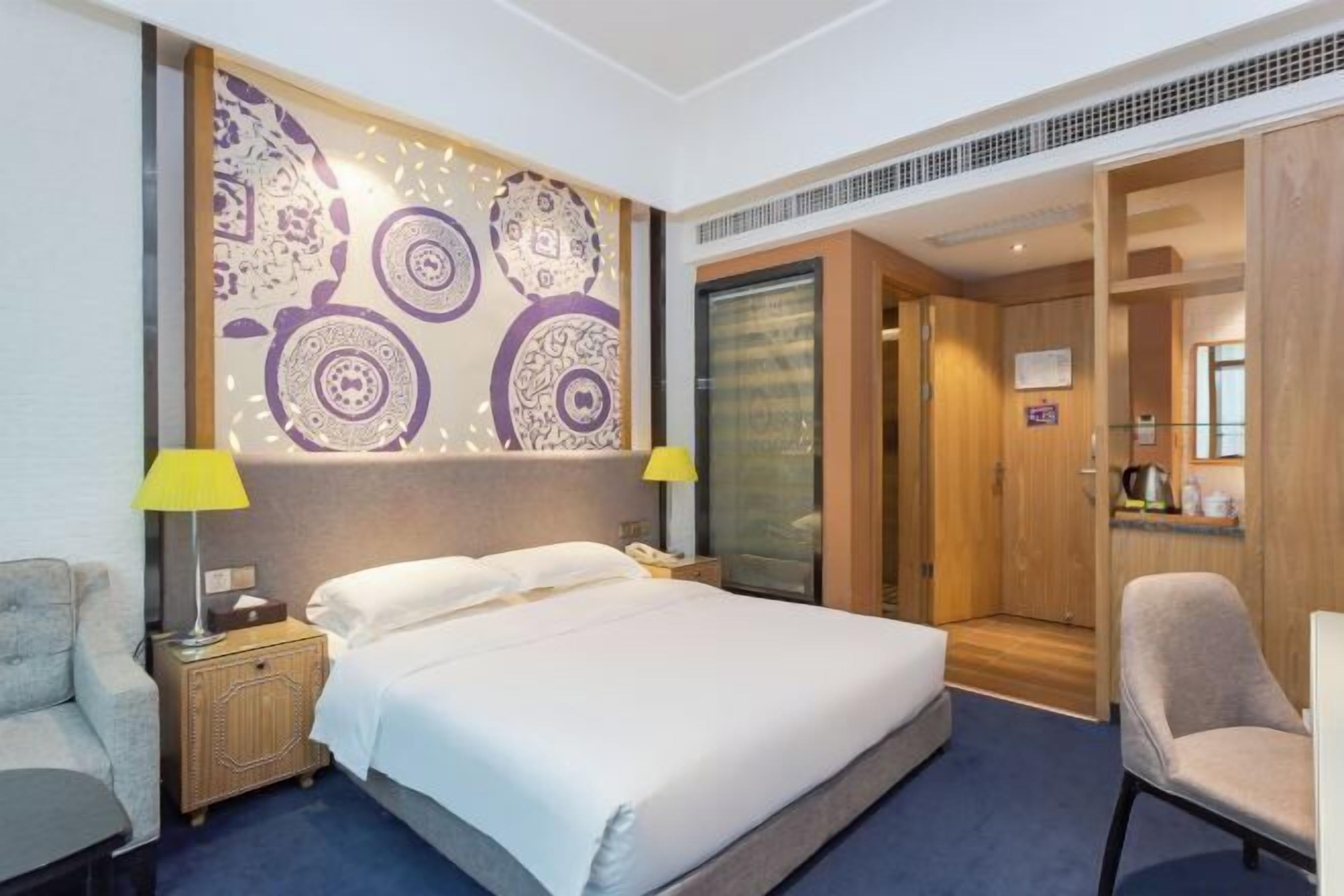 Habitación de hotel con una cama grande, una mesita de noche, una silla, una pared con diseños decorativos y un armario de madera.
