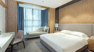A hotel room with a bed, a desk, a chair, a nightstand, and a window with curtains.