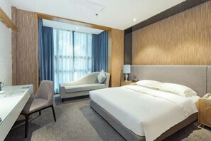Ein Hotelzimmer mit Bett, Schreibtisch, Stuhl, Nachttisch und einem Fenster mit Vorhängen.