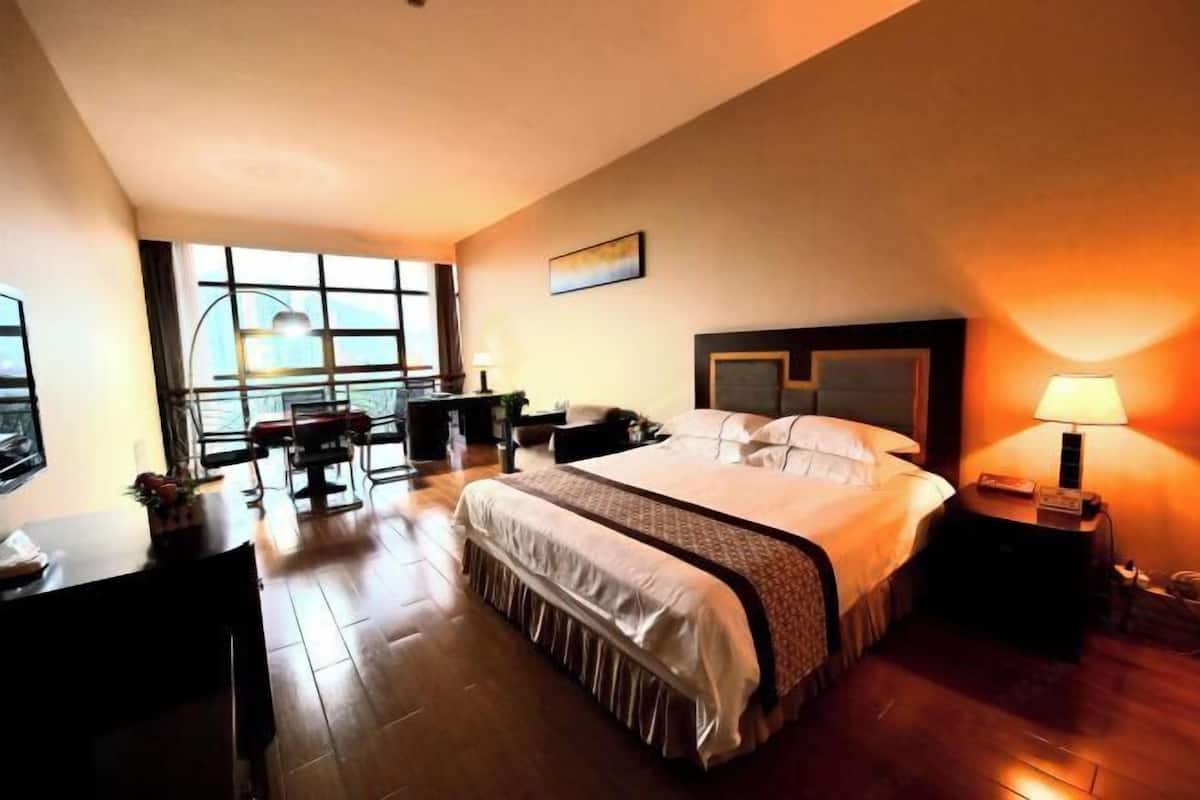 Une chambre d’hôtel avec un grand lit, un bureau, une chaise, une télévision et une fenêtre donnant sur un beau paysage.