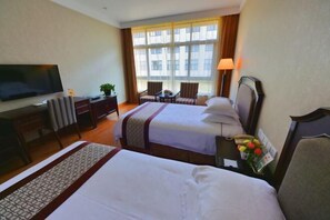 Quarto de hotel com duas camas, televisão, escrivaninha, abajur e janela com vista para edifícios.