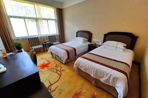 Quarto de hotel com duas camas, uma escrivaninha, uma cadeira e vista para o exterior através de amplas janelas.