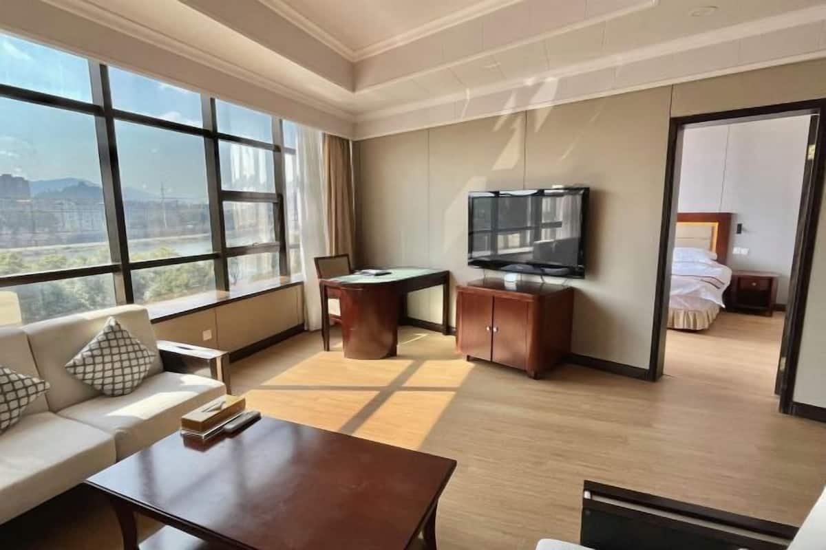 Une chambre d’hôtel avec une grande fenêtre, un canapé, un bureau, une télévision et un lit.