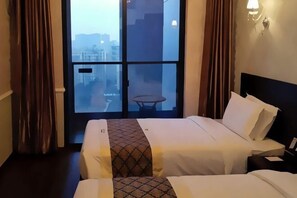 Quarto de hotel com duas camas, vista pela janela ampla e uma pequena mesa junto à janela.