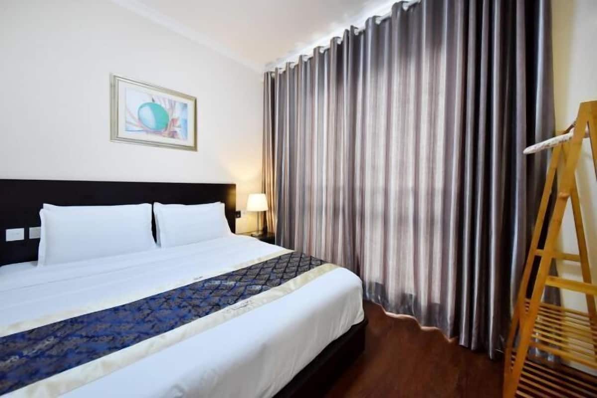 Una habitación de hotel con cama, cortinas, un cuadro en la pared y una escalera de madera.