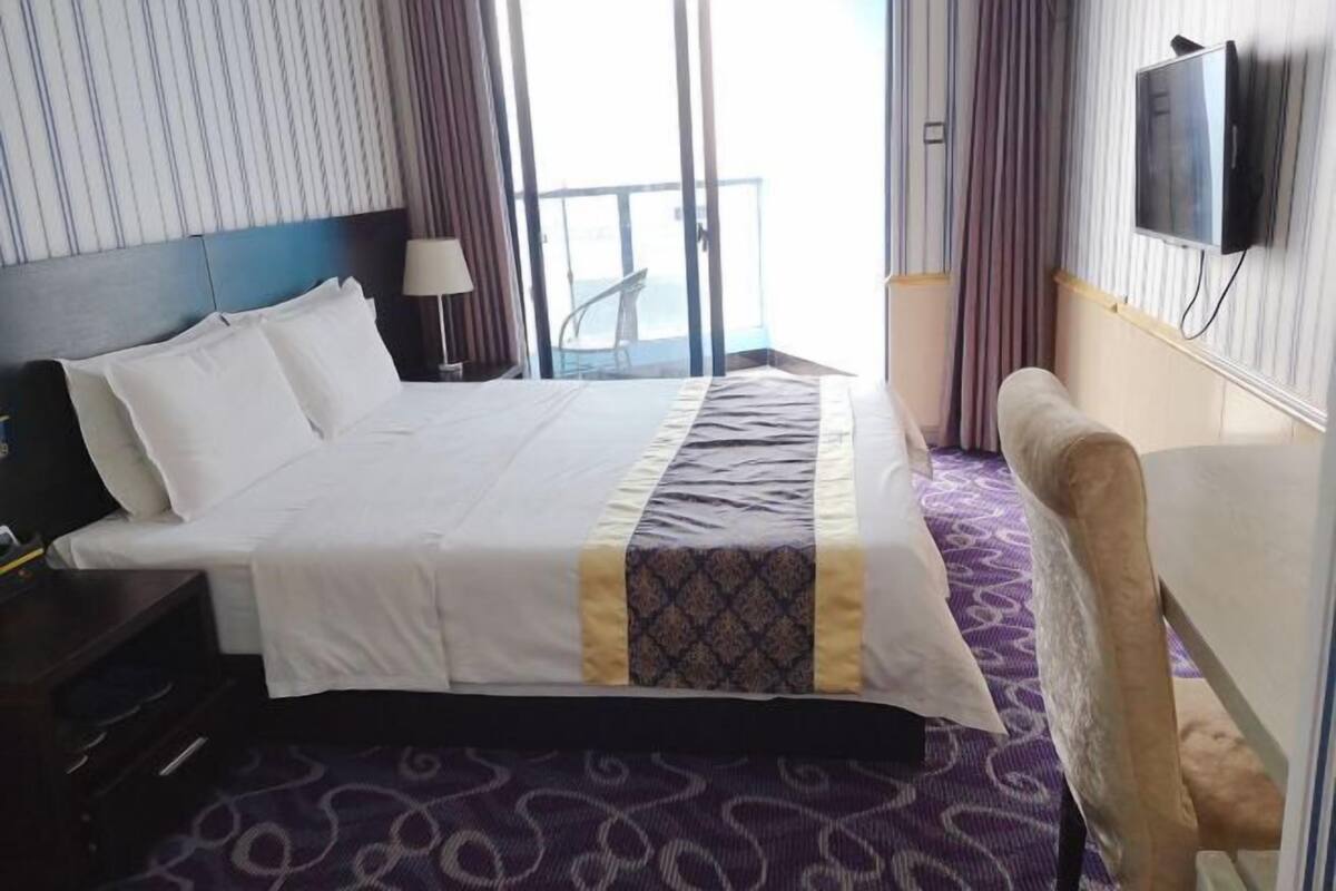 Habitación de hotel con una cama grande, un escritorio, una silla, un televisor y un balcón con vistas.