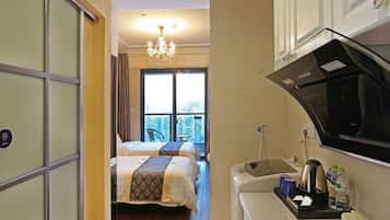 A hotel room with a bed, a kitchenette, a window with a view, and a chandelier.
