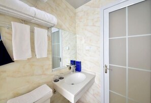 Un baño con lavamanos blanco, espejo y toallero.