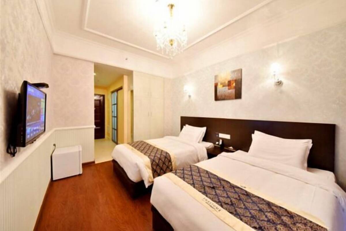 Habitación de hotel con dos camas, televisor, candelabro y un cuadro en la pared.