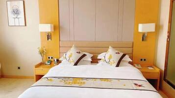 A hotel room with a large bed, two bedside tables, a nightstand, a wall-mounted lamp, and a framed picture on the wall.