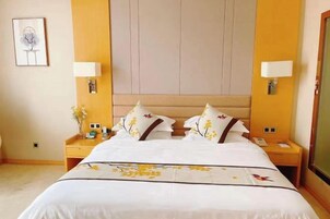 A hotel room with a large bed, two bedside tables, a nightstand, a wall-mounted lamp, and a framed picture on the wall.