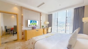 Een hotelkamer met een bed, bureau, stoel, televisie en een groot raam.
