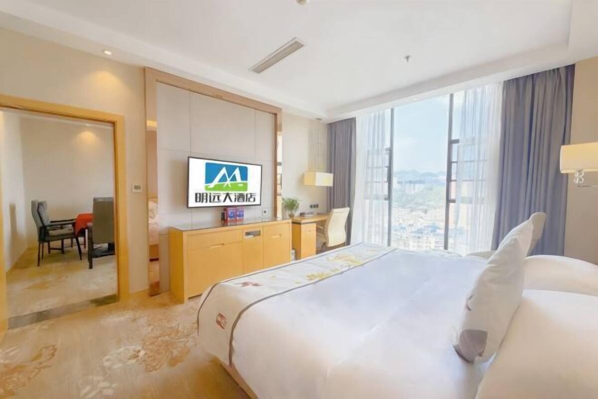 Ein Hotelzimmer mit Bett, Schreibtisch, Stuhl, Fernseher und einem großen Fenster.