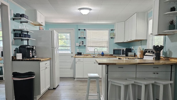 A kitchen with white cabinets, a wooden countertop, a sink, a stove, and a trash can. - "Salty Dogs: Your Dog-Friendly Haven for Coastal Getaways!" (Oak Island)
