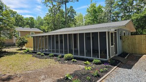 A single-story house with a covered patio area, surrounded by a wooden fence and a garden with various plants. - "Salty Dogs: Your Dog-Friendly Haven for Coastal Getaways!" (Oak Island)