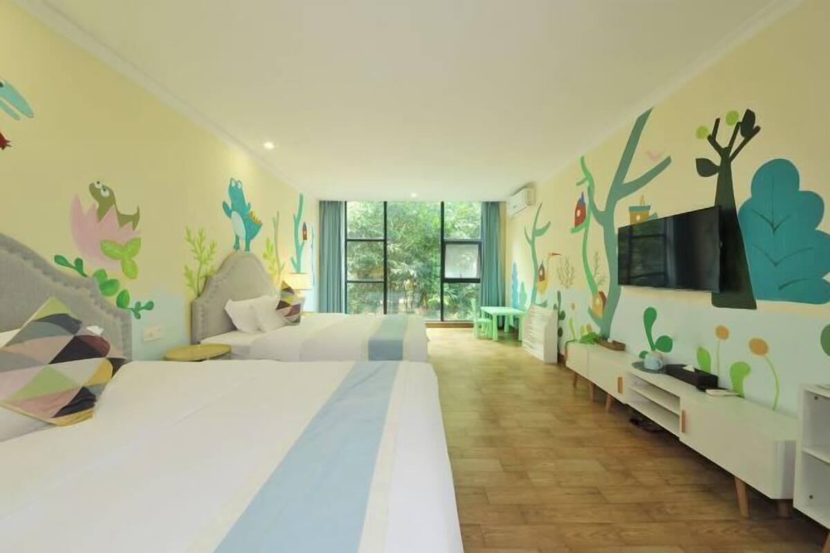 Habitación de hotel con dos camas, un televisor, una ventana y una pared decorada con murales de plantas y animales.