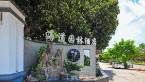 Entrada de hotel con fachada de piedra, un árbol grande y un letrero con caracteres chinos.