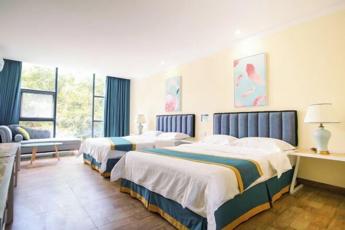Habitación de hotel con dos camas, un escritorio, una silla y ventanas amplias con cortinas.