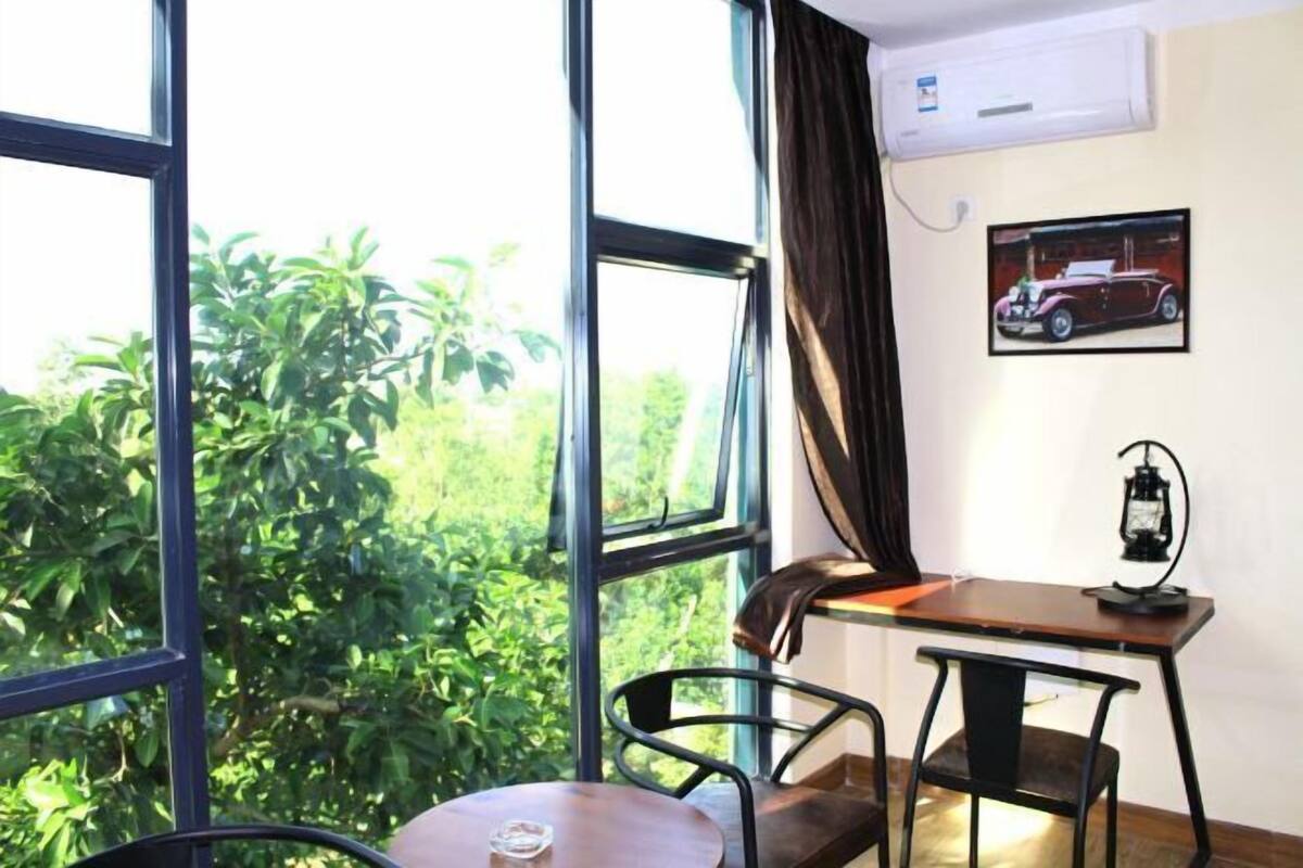 Una habitación con un ventanal grande, una mesa, dos sillas, un aire acondicionado instalado en la pared y un cuadro enmarcado.