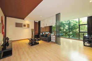 Una sala de estar moderna con un sofá, una mesa de centro y un televisor. Hay un ventanal con vistas a zonas verdes.